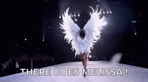 A Woman In A White Angel Costume Is Walking Down A Runway With The Words `` There Goes Melissa '' . GIF