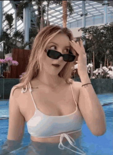 a woman in a white bikini and sunglasses is standing in a pool