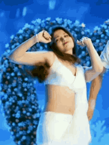 A Woman In A White Bra And White Skirt Is Dancing In Front Of A Flower Arrangement . GIF