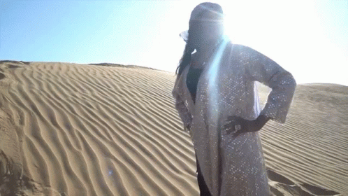 A Woman In A White Coat Stands In The Sand GIF