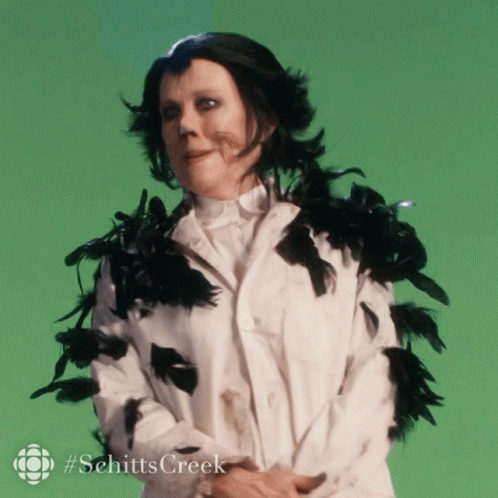 A Woman In A White Coat With Black Feathers Around Her Neck And Collar GIF