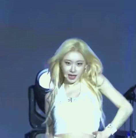A Woman In A White Crop Top Is Dancing On A Stage . GIF