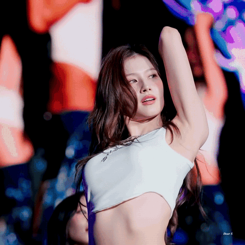 A Woman In A White Crop Top Is Standing On A Stage With Her Arms Outstretched GIF