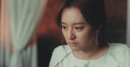 A Woman In A White Dress And Earrings Is Looking Down GIF