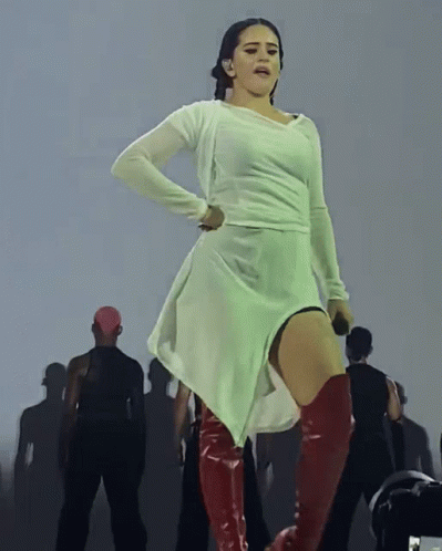 A Woman In A White Dress And Red Boots Is Standing On A Stage GIF