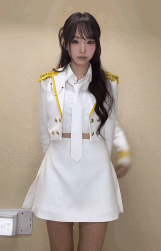 A Woman In A White Dress And Tie Is Standing In Front Of A Wall That Says Exit GIF