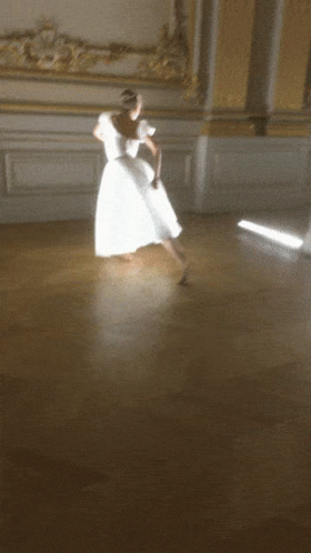 A Woman In A White Dress Dancing On A Wooden Floor GIF