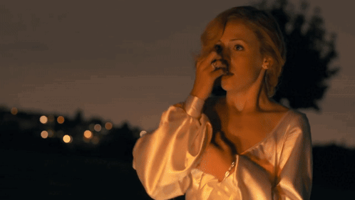 A Woman In A White Dress Is Covering Her Face With Her Hand GIF