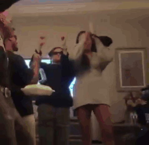 A Woman In A White Dress Is Dancing In A Living Room With Other People . GIF