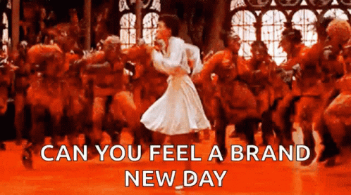 A Woman In A White Dress Is Dancing In Front Of A Crowd With The Words " Can You Feel A Brand New Day " Below Her GIF