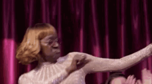 A Woman In A White Dress Is Dancing In Front Of A Red Curtain . GIF