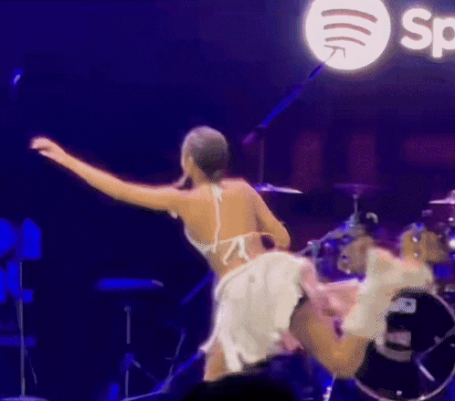 A Woman In A White Dress Is Dancing On A Stage In Front Of A Spotify Logo GIF