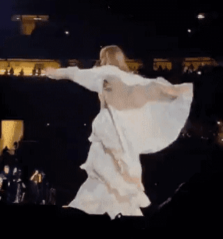 A Woman In A White Dress Is Dancing On A Stage With Her Wings Outstretched . GIF