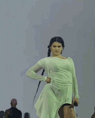 A Woman In A White Dress Is Dancing On Stage . GIF