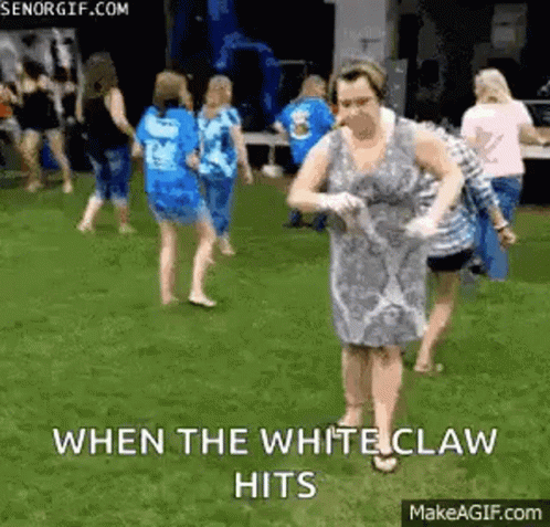 A Woman In A White Dress Is Dancing On The Grass With A Group Of People . GIF