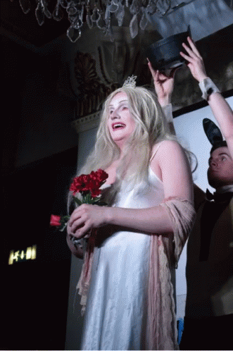 A Woman In A White Dress Is Holding A Bouquet Of Red Flowers GIF
