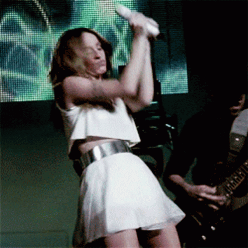A Woman In A White Dress Is Holding A Microphone GIF