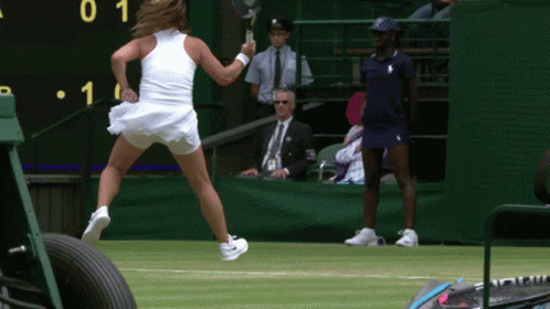 A Woman In A White Dress Is Holding A Tennis Racquet In Front Of A Scoreboard With The Number 1 On It GIF