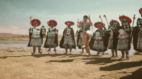 a woman in a white dress is jumping in the air in front of a group of people in traditional costumes