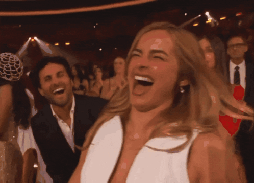 A Woman In A White Dress Is Laughing In A Crowded Room GIF