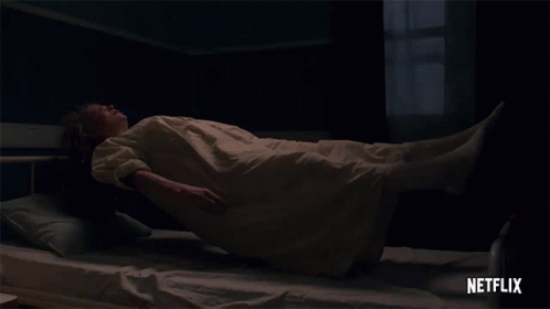 A Woman In A White Dress Is Laying On A Bed With A Netflix Logo Behind Her GIF