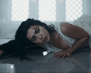 A Woman In A White Dress Is Laying On The Floor Looking At The Camera GIF