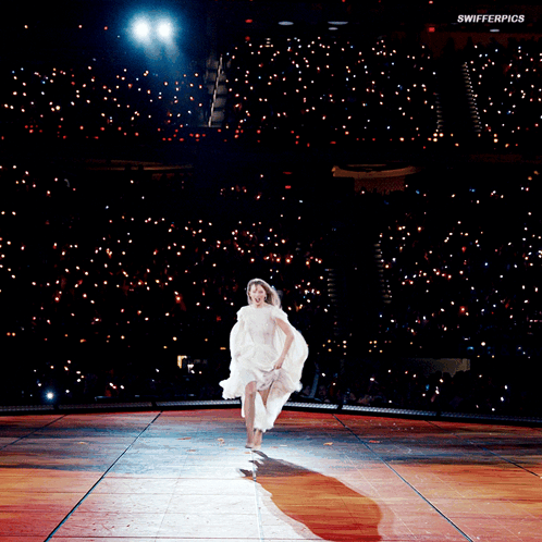 A Woman In A White Dress Is Running On A Stage With Swifterpics Written On The Bottom Of The Image GIF