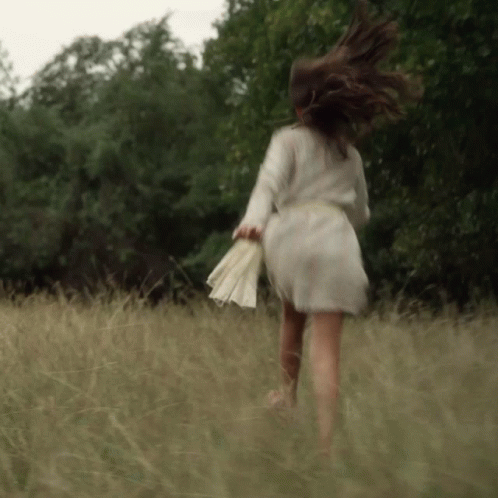 A Woman In A White Dress Is Running Through Tall Grass GIF