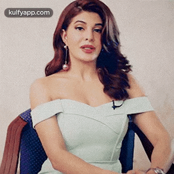 A Woman In A White Dress Is Sitting In A Chair And Making A Funny Face . GIF