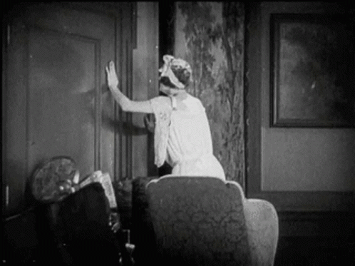 A Woman In A White Dress Is Sitting In A Chair In A Living Room . GIF