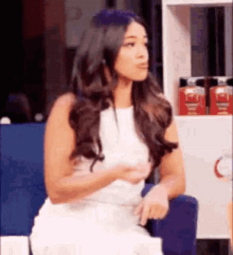 A Woman In A White Dress Is Sitting In A Chair In Front Of A Shelf . GIF
