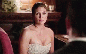 A Woman In A White Dress Is Sitting Next To A Man In A Suit And Looking At Him . GIF