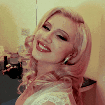 A Woman In A White Dress Is Smiling And Looking At The Camera GIF