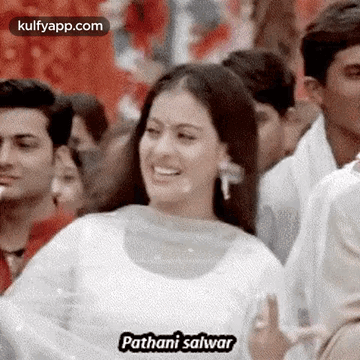 A Woman In A White Dress Is Smiling In Front Of A Crowd . GIF