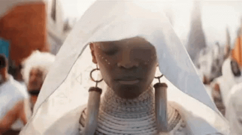 A Woman In A White Dress Is Standing In A Crowd Of People . GIF