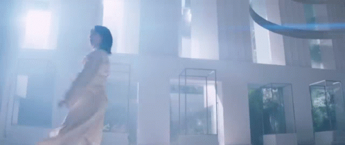 a woman in a white dress is standing in a room with a lot of windows .