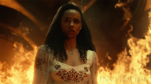 A Woman In A White Dress Is Standing In Front Of A Fire And The Word Invitation Is Visible GIF
