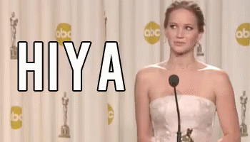 A Woman In A White Dress Is Standing In Front Of A Microphone With The Word Hiya Written On It GIF