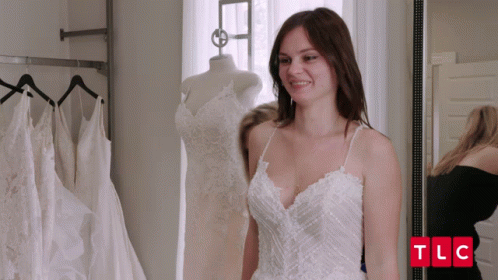 A Woman In A White Dress Is Standing In Front Of A Mirror With Tlc Written In Red Letters GIF