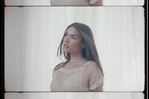 A Woman In A White Dress Is Standing In Front Of A White Curtain GIF