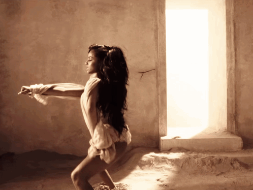 A Woman In A White Dress Is Standing In Front Of A Window GIF