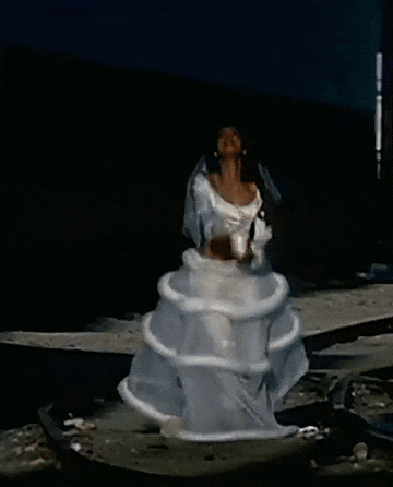 A Woman In A White Dress Is Standing In The Water With Her Arms In The Air GIF