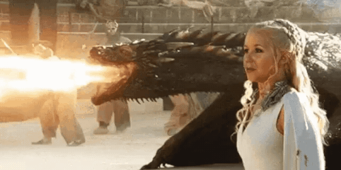 A Woman In A White Dress Is Standing Next To A Dragon That Is Shooting Fire . GIF