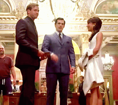 A Woman In A White Dress Is Standing Next To A Man In A Suit And Tie GIF