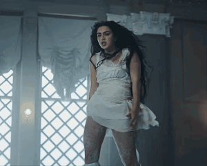 A Woman In A White Dress Is Standing Next To A Window GIF