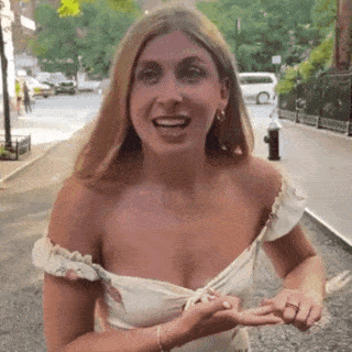 A Woman In A White Dress Is Standing On A Sidewalk . GIF