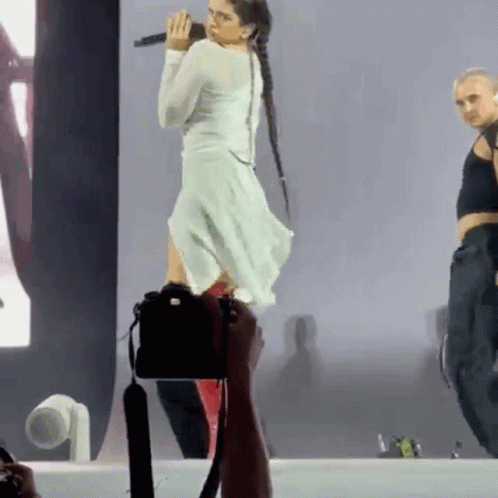 A Woman In A White Dress Is Standing On A Stage With A Microphone In Her Hand . GIF