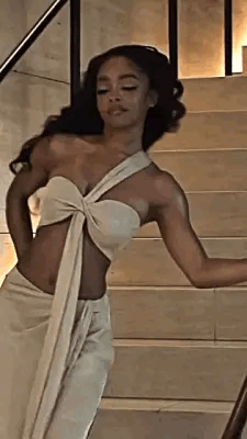 A Woman In A White Dress Is Standing On Stairs . GIF