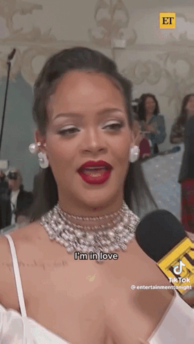 A Woman In A White Dress Is Talking Into A Microphone . GIF