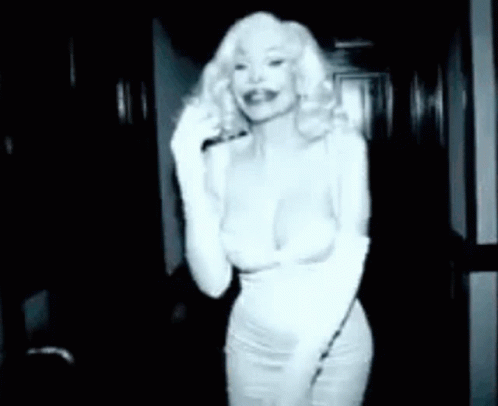 A Woman In A White Dress Is Talking On A Phone In A Dark Room . GIF
